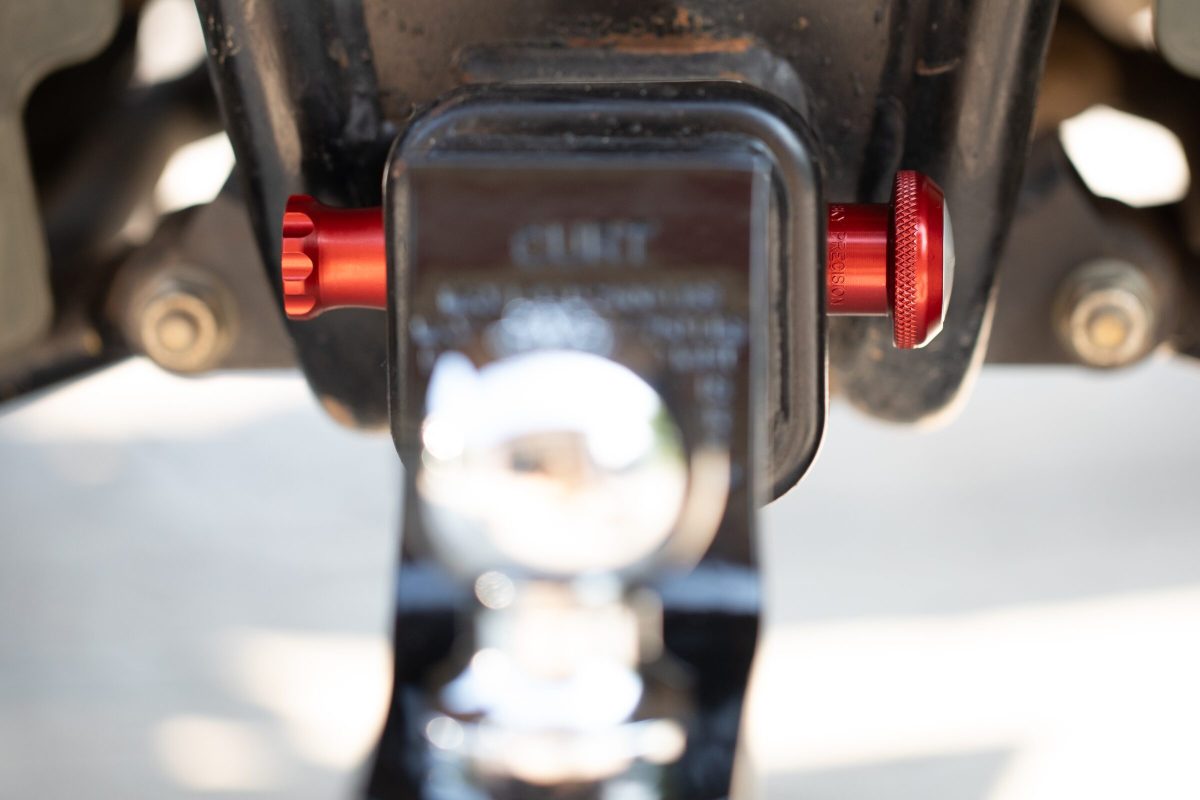 Both ends of the PinUltimate ATV Hitch Pin seated through a ball mount, showing knob and quick-release knob